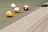 Close-up of a pool table corner with four billiard balls on a green felt surface and a light wood grain rail.
