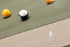 Close-up of a billiards table corner with a green felt surface, wooden side rail, and several pool balls including a yellow ball, a blue-and-white numbered ball, and part of an orange ball.