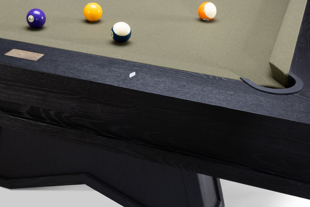 Close-up of a pool table corner with a dark wood frame, green felt surface, and several billiard balls including a purple 9-ball, yellow 8-ball, blue 7-ball, and orange/white 6-ball.