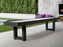 American Heritage Lanai 9' Outdoor Shuffleboard Table in Obsidian Black on a patio with greenery.