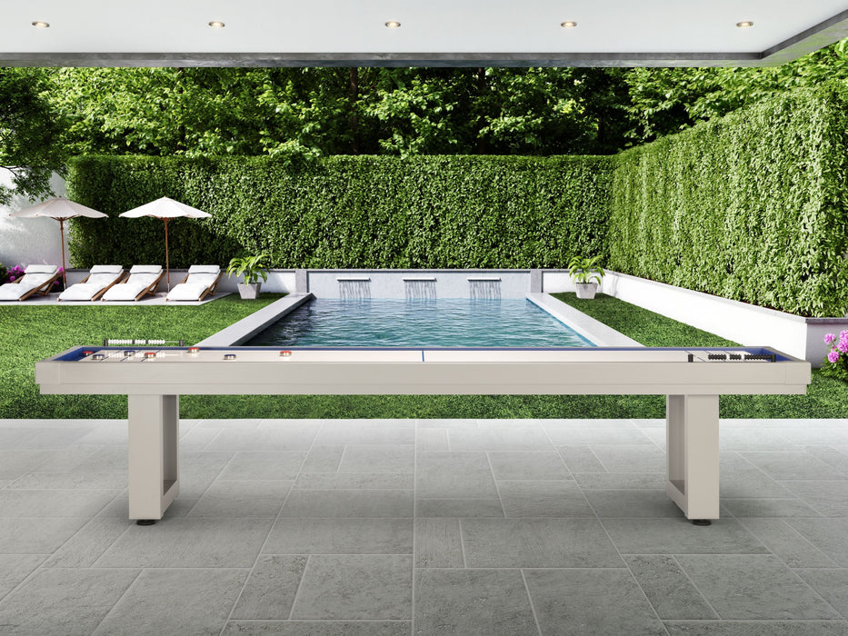 American Heritage Lanai 9' Outdoor Shuffleboard Table in Oyster Grey on patio by pool and hedges.
