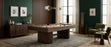 A dark wood pool table with colorful billiard balls on a gray patterned rug in a modern, stylishly decorated room with dark green walls, wooden paneling, and green armchairs.