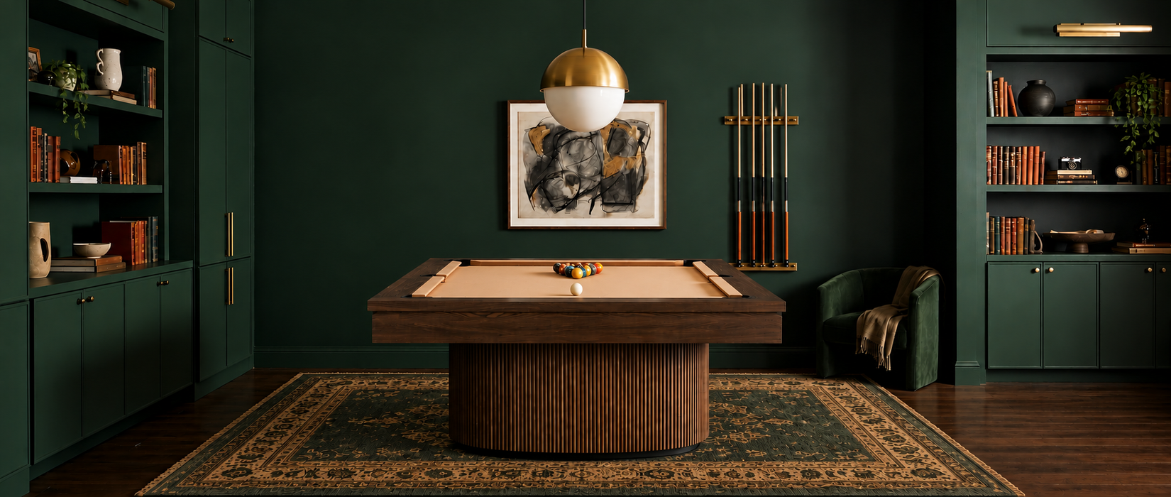 A dark wood pool table with a beige felt surface sits in a styled room with deep green walls, built-in bookshelves, a hanging gold-and-white globe light, and a patterned rug.