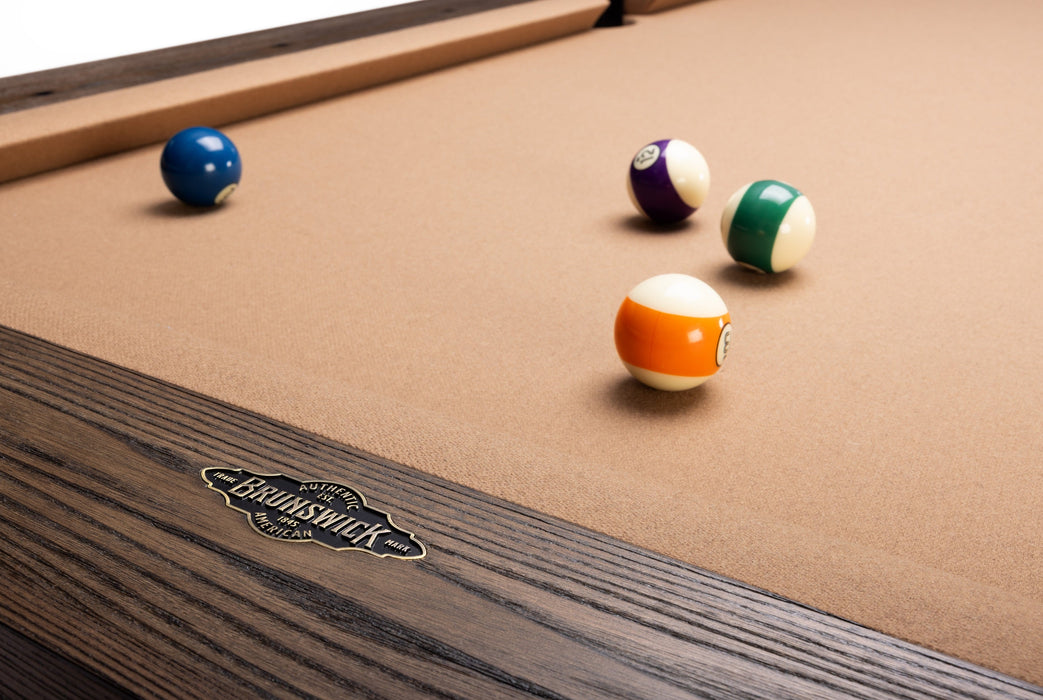 Close-up of a BenNSWIK pool table with a tan felt surface and dark wood frame, showing several billiard balls on the table.