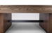 Close-up of a modern wooden table or console table showing the thick wood grain top, fluted side supports, and a black metal shelf rail underneath, photographed against a clean white studio background.