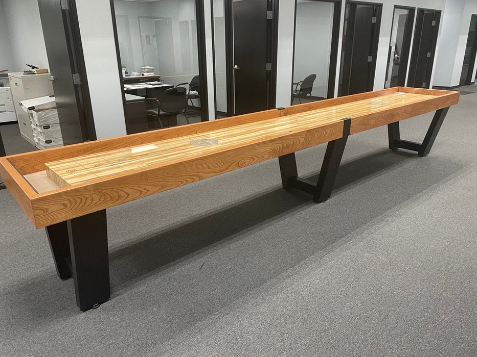 A Champion 9' Fremont Shuffleboard Table with black legs is in an office hallway on carpet.